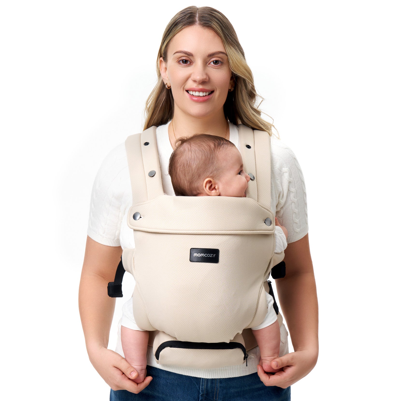 Momcozy baby carrier in beige, worn by a smiling woman, securely holding an infant. Ergonomic design for comfort and support.