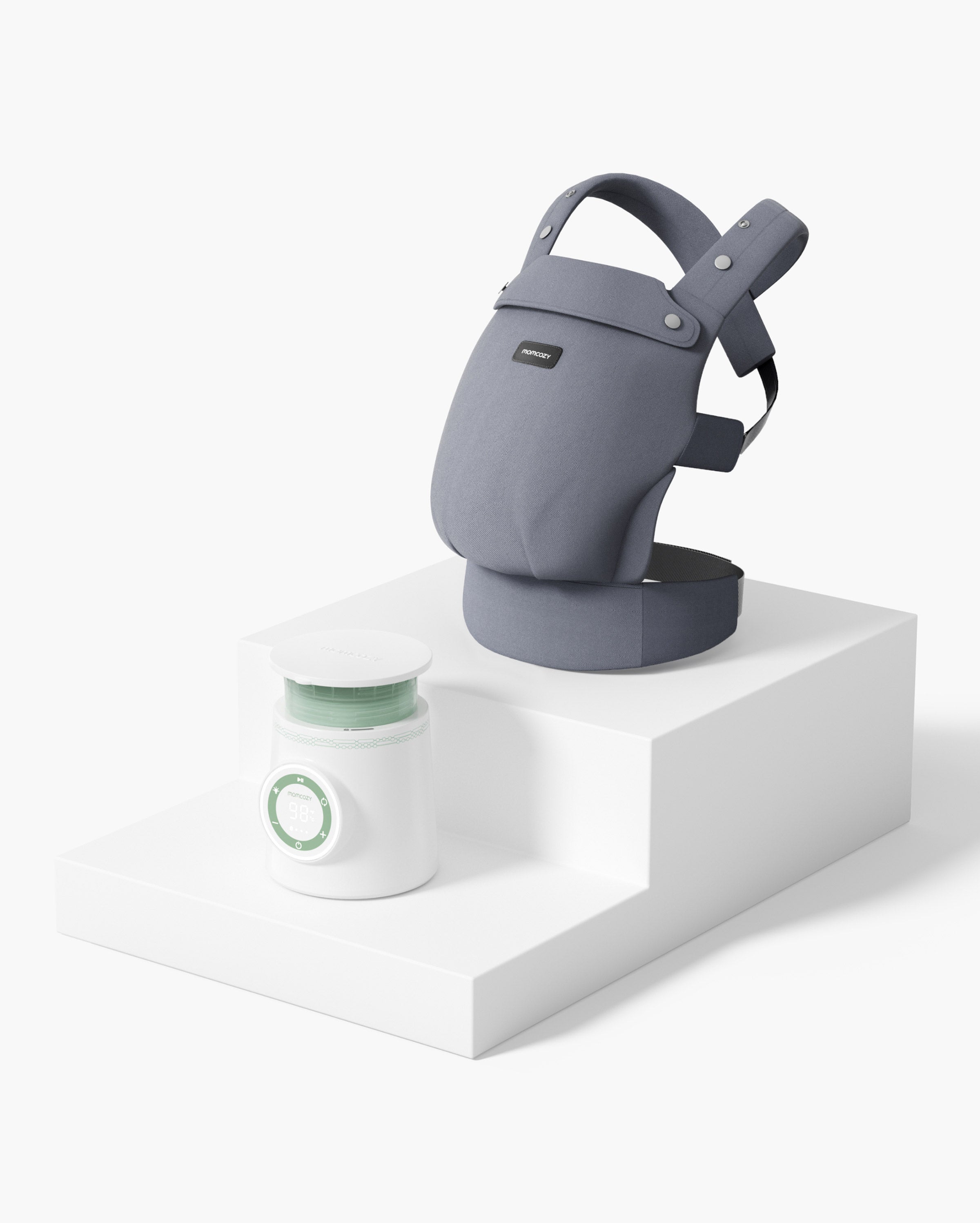 Momcozy Baby Carrier Bundle including a gray baby carrier and a white baby bottle warmer placed on a stepped white platform