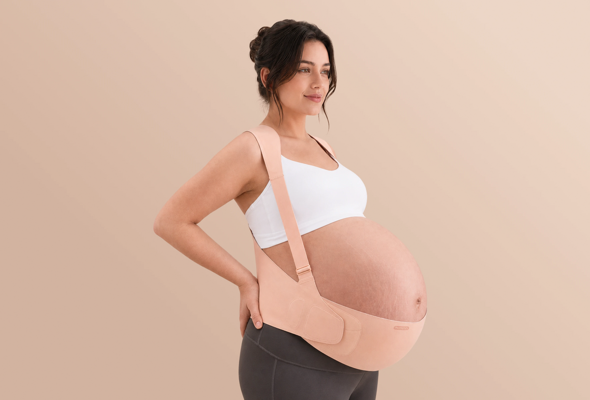 Side view of a pregnant woman wearing the oyster pink Momcozy maternity belly band with shoulder straps.