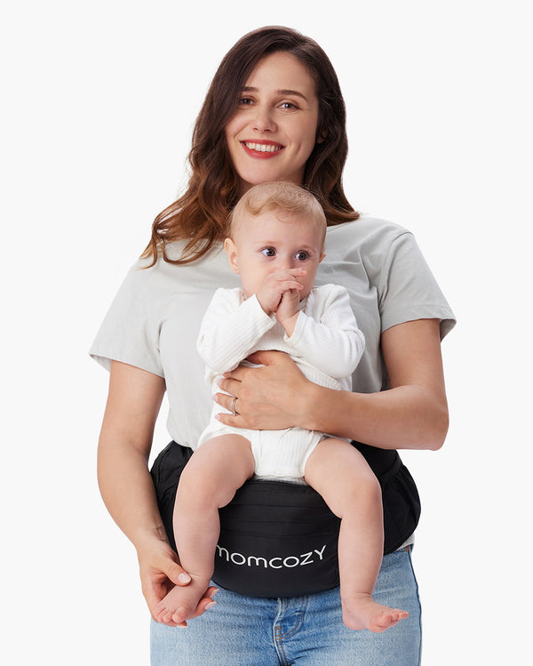 Mother holding baby seated on black Momcozy baby hip seat carrier, both smiling.