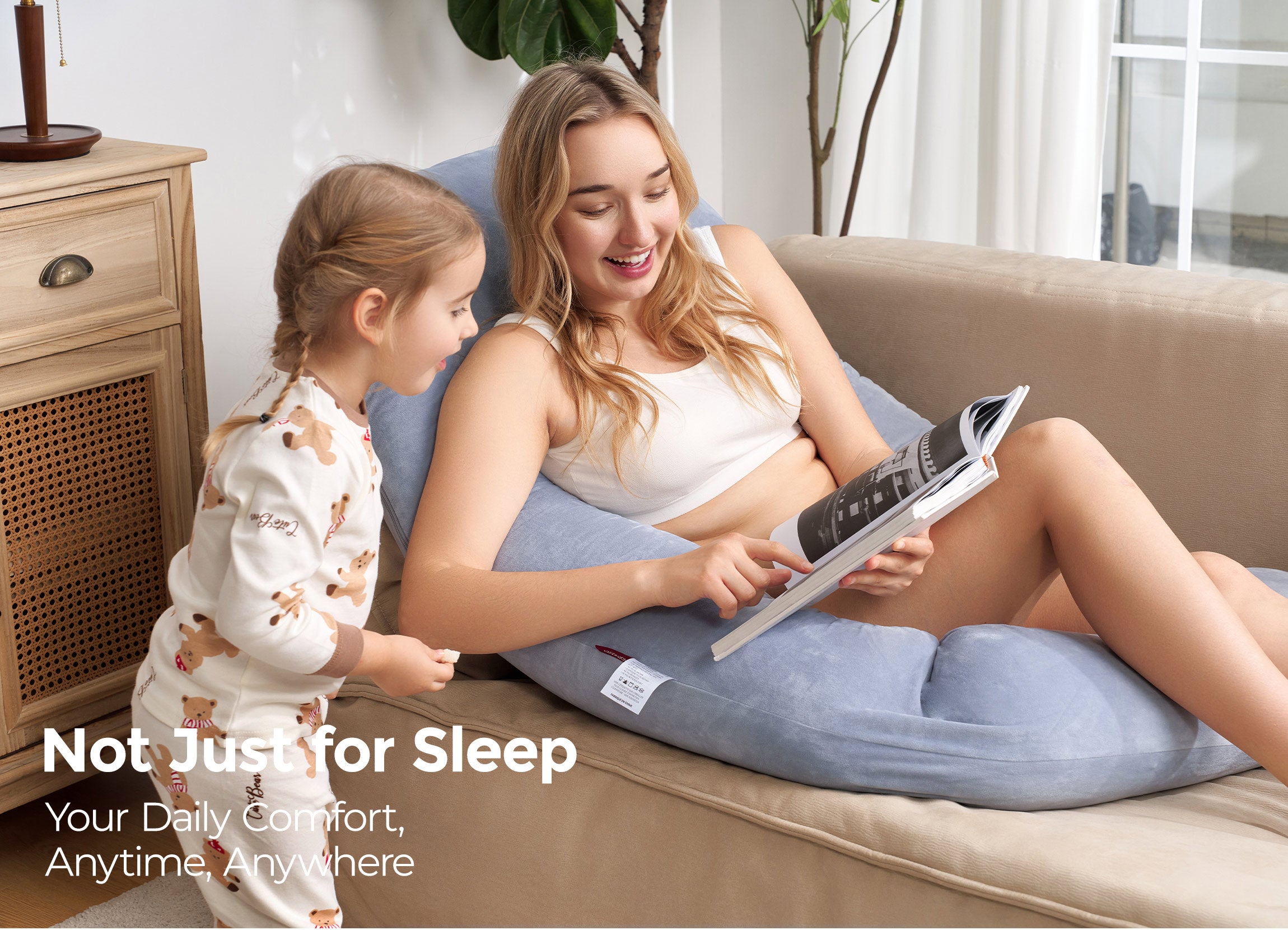 Momcozy Dreamlign pregnancy pillow used by a pregnant woman, providing all-day comfort, reading a book with a child.