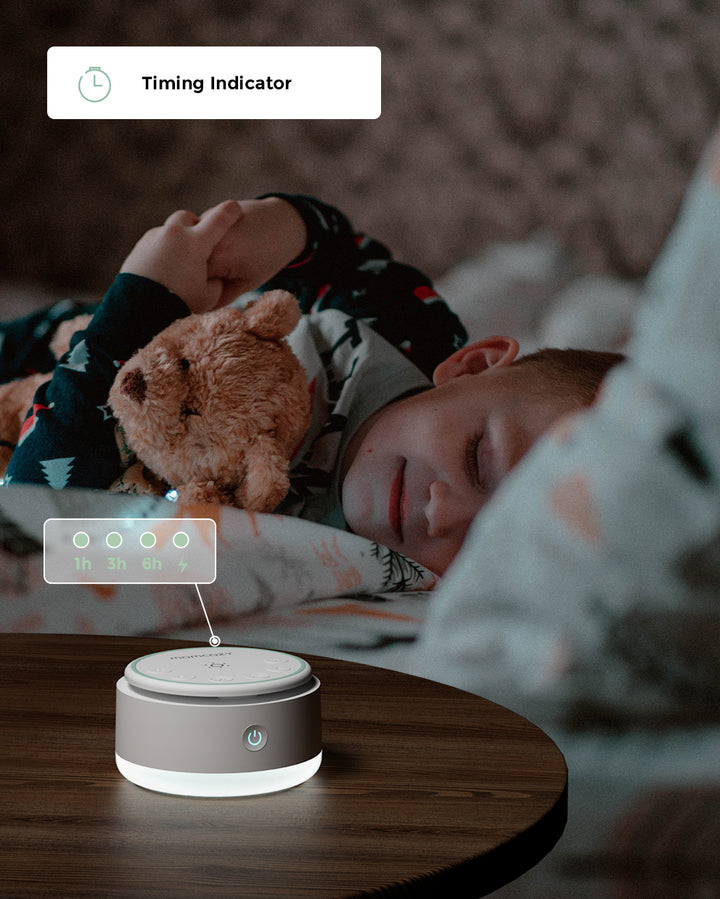 Child sleeping with a teddy bear while a portable baby sound machine with timing indicator options is on a nearby table.