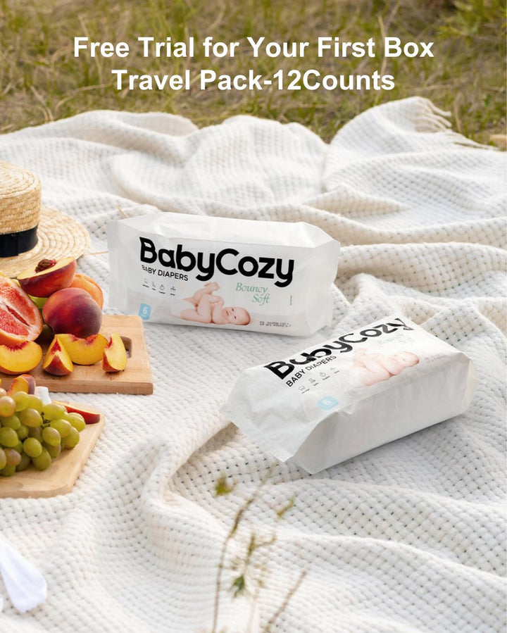 Outdoor scene with BabyCozy diapers on a blanket, surrounded by fresh fruits and a hat, promoting a free trial for your first box travel pack of 12 counts.