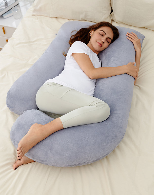 Maman utilisant un coussin de grossesse Momcozy en U dans un intérieur naturel