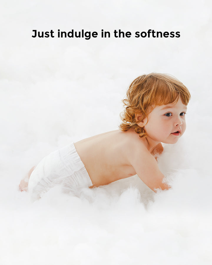 Baby wearing BabyCozy diaper crawling on cloud-like soft surface with text 'Just indulge in the softness'