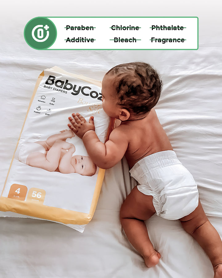 Baby wearing a BabyCozy diaper touching a package of BabyCozy Softest Diapers, showing it is free of parabens, chlorine, phthalates, additives, bleach, and fragrance