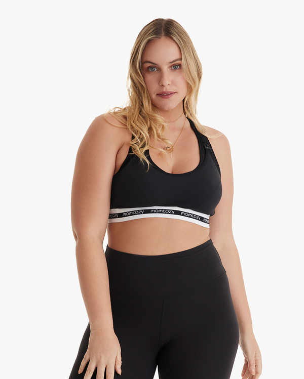 Woman modeling Momcozy black low-impact nursing sports bra with branded elastic band and matching black high-waisted leggings